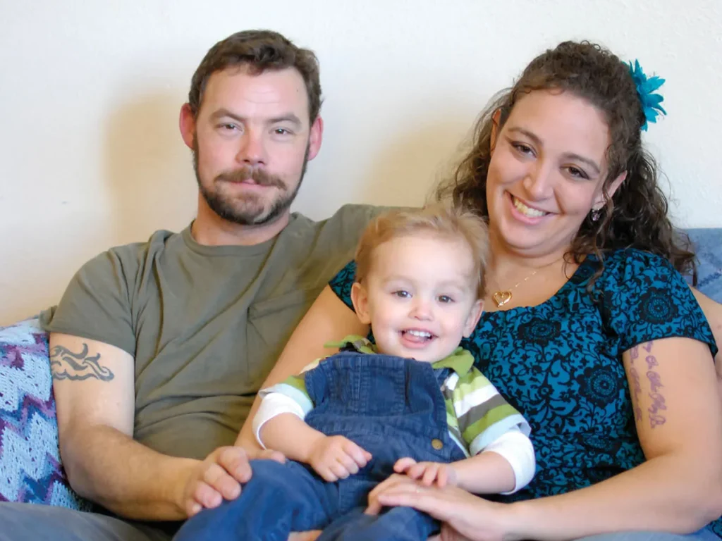 A young couple and toddler playfully sit on a couch.