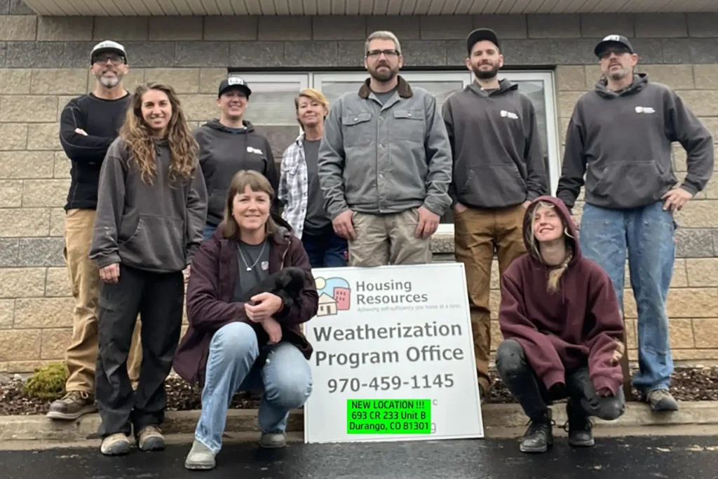 A group of volunteers holding a sign that reads "Weatherization Program Office" outside on a rainy day.