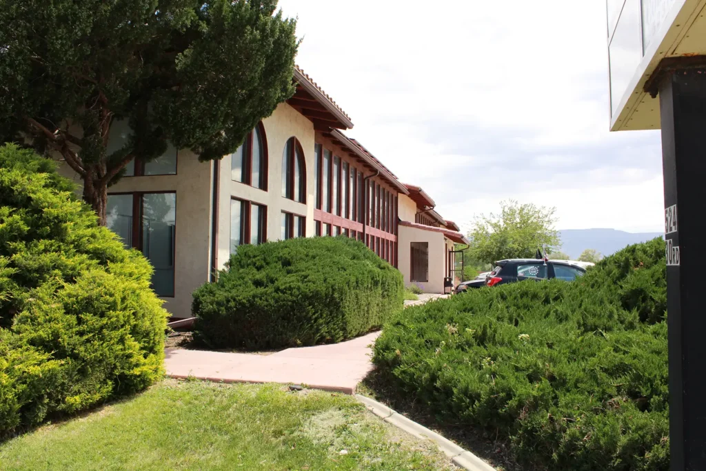 An outside view of the red and beige Housing Resources of Western Colorado Office and surrounding green bushes and lawn.